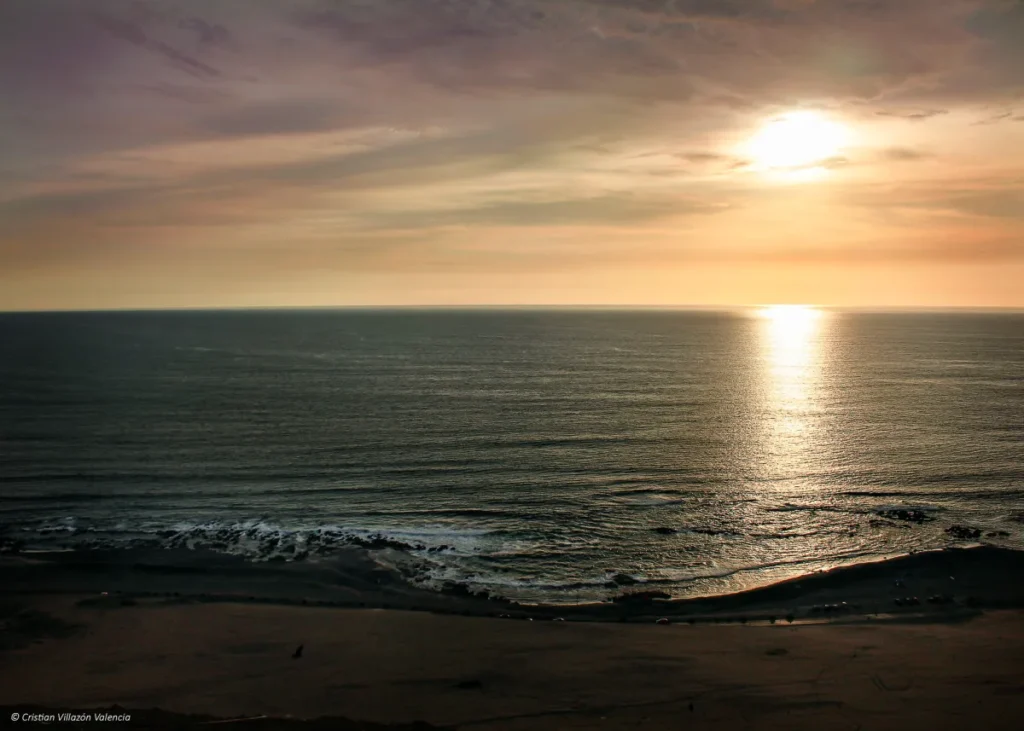 Vista de una playa con arena oscura al atardecer, creando un paisaje único y tranquilo junto al mar